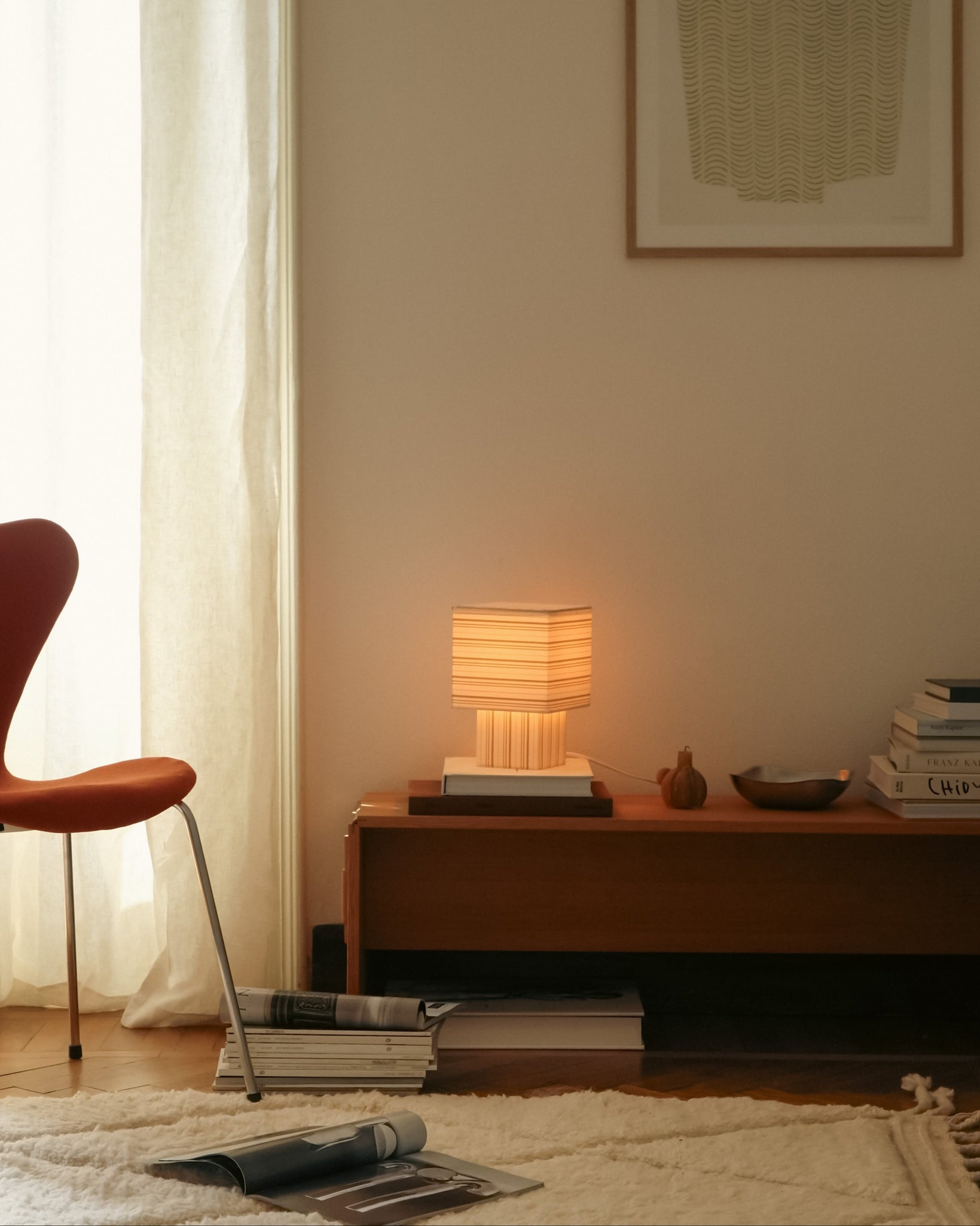 Living room with a lamp on a wooden side table, books, and a chair.